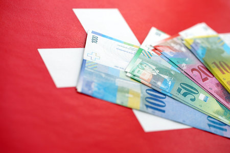 Swiss franc banknotes and flag. The current francs money bills lies on flag in big amount. The concept of business and investment in Switzerlandの写真素材