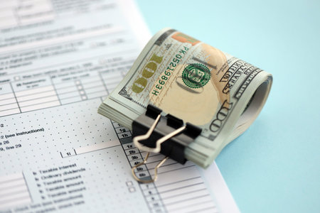 Big amount of United States USD dollar bills banknotes on table with 1040 individual income tax return form. Concept of taxation and accounting in United Statesの写真素材