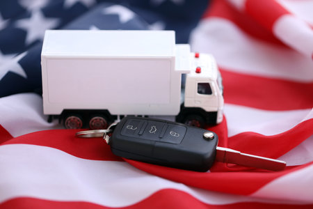 Ignition keys with remote control buttons and toy truck on United States flag. Concept of car driving in USA. Vehicle ownershipの写真素材