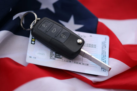 Ignition keys with remote control buttons and driver license card on United States flag. Concept of...
