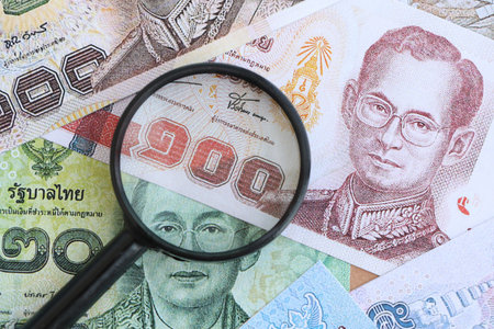 Thai baht currency money bills and magnifying glass close up. The concept of financial monitoring...