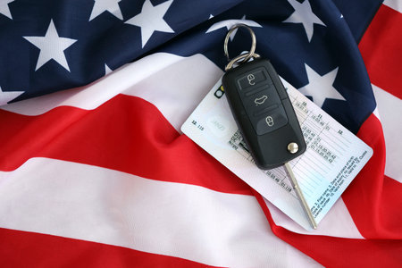 Ignition keys with remote control buttons and driver license card on United States flag. Concept of car driving in USA. Vehicle ownershipの写真素材