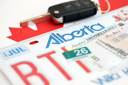 Alberta canadian car license plate and ignition key on flag of Canada close up. Driving permit and...