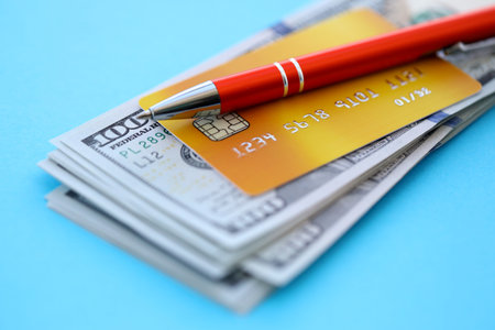 Credit card and pen with US dollar currency money bills banknotes on light blue background. Business, financial operations and accounting in United States of Americaの写真素材