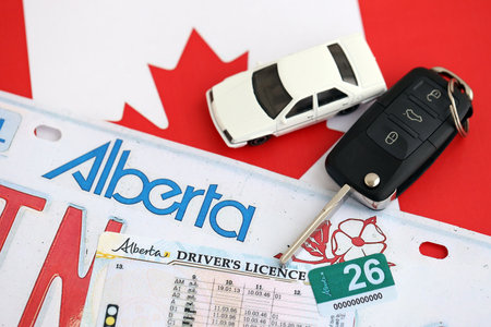 Alberta canadian car license plate and ignition key on flag of Canada close up. Driving permit and registration conceptの写真素材