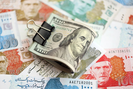 Roll of US dollar bills lies on big amount of Pakistan rupees banknotes close up. American money bunch lies on Pakistan money bills. The concept of economics and currency exchange in Pakistanの写真素材