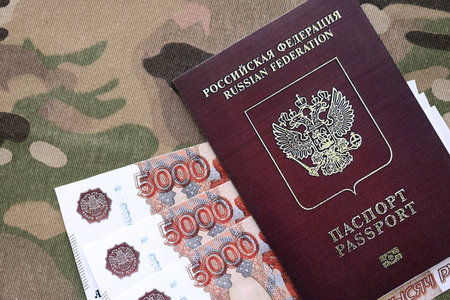 Russian passport with money on multicam camouflage fabric close up. Concept of russian army funds and invasion to Ukraineの写真素材