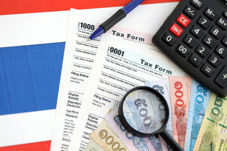 Thai baht money bills and calculator with tax form on flag close up. Taxation and accounting conceptの写真素材