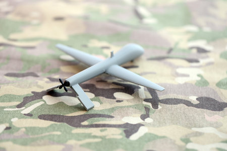Unnamed grey toy drone model on camouflage fabric close up. Observation drone for intelligence tasksの写真素材