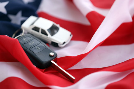 Ignition keys with remote control buttons and toy car on United States flag. Concept of car driving in USA. Vehicle ownershipの写真素材