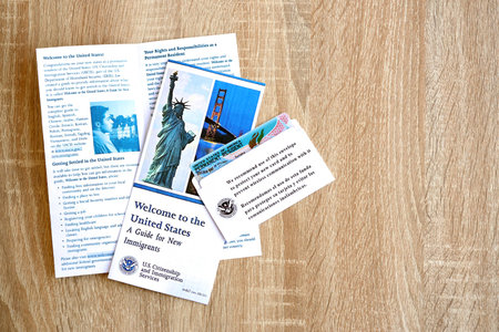 KYIV, UKRAINE - AUGUST 31, 2025 Permanent resident green card in envelope and guide for new immigrants lies on wooden table close upのeditorial素材