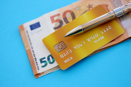 Credit card and pen with euro currency money bills banknotes on light blue background. Business, financial operations and accounting in European Unionの写真素材