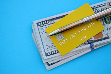 Credit card and pen with US dollar currency money bills banknotes on light blue background. Business, financial operations and accounting in United States of Americaの写真素材