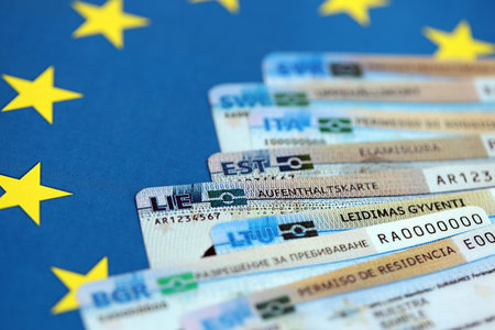 Permanent resident or residence permit cards lies on European Union flag. Paper specimen cards close...