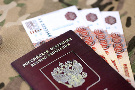 Russian passport with money on multicam camouflage fabric close up. Concept of russian army funds...