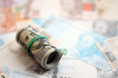 Roll of US dollar bills lies on big amount of Brazilian reais banknotes close up. American money roll lies on Brazil money bills. The concept of economics and currency exchange in Brazilの写真素材
