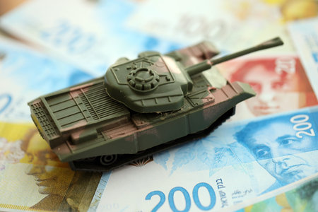 Israel New Shekels banknotes and toy tank. The current Israel money bills and tank lies on table in big amount. The concept of army funds and weapons sales in Israelの写真素材