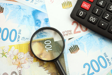 Israel New Shekels banknotes and calculator with magnifying glass. The current Israel money bills...