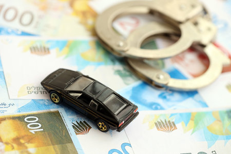 Israel New Shekels banknotes and toy car with handcuffs. The current Israel money bills and black car with cuffs lies on table in big amount.の写真素材