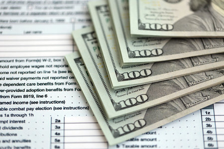 Big amount of United States USD dollar bills on table with 1040 individual income tax return form....