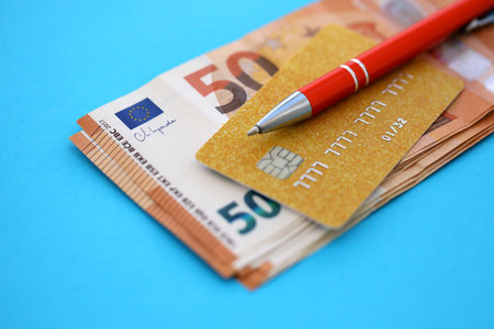 Credit card and pen with euro currency money bills banknotes on light blue background. Business, financial operations and accounting in European Unionの写真素材