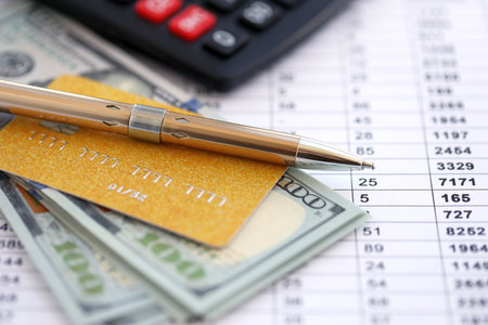 Credit card and pen with US dollar currency money bills banknotes on calculations document background. Business, financial operations and accounting in United States of Americaの写真素材