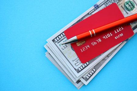 Credit card and pen with US dollar currency money bills banknotes on light blue background. Business, financial operations and accounting in United States of Americaの写真素材