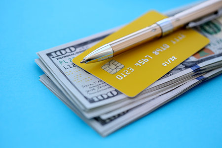 Credit card and pen with US dollar currency money bills banknotes on light blue background. Business, financial operations and accounting in United States of Americaの写真素材