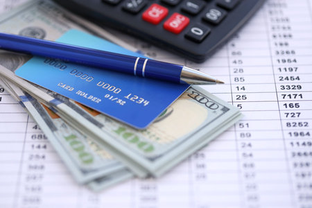 Credit card and pen with US dollar currency money bills banknotes on calculations document background. Business, financial operations and accounting in United States of Americaの写真素材