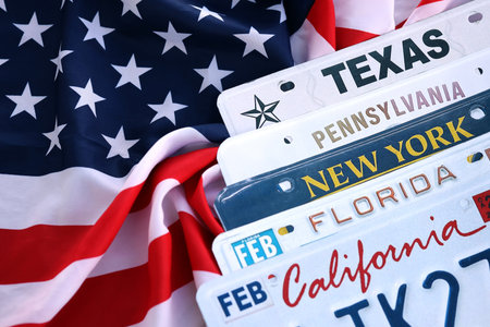 Old US car license plates with various state names on USA flag. Concept of driving in United States. Reaching a car registrationの写真素材