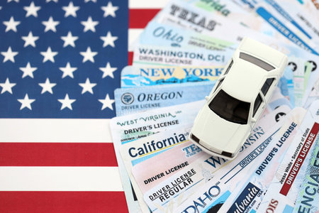 Toy car on big amount of driving licenses from different USA states on flag close up. Stack of driving license specimen cardsの写真素材