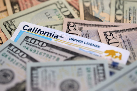 California state driving license among big amount of US dollar bills close up