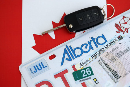 Alberta canadian car license plate and ignition key on flag of Canada close up. Driving permit and registration concept