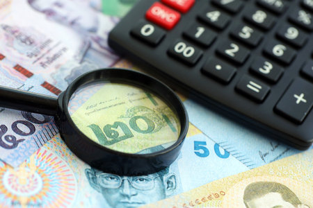 Thai baht currency money bills and calculator with magnifying glass close up. The concept of...