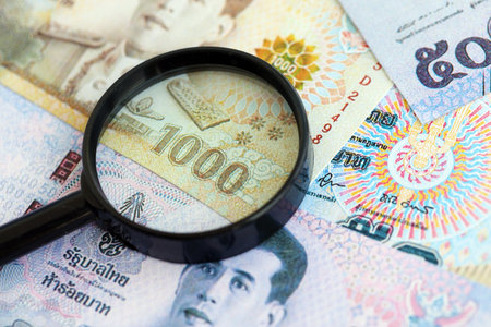 Thai baht currency money bills and magnifying glass close up. The concept of financial monitoring...
