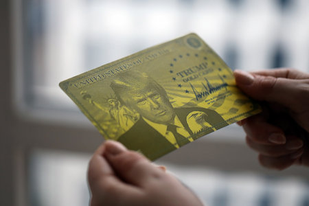 KYIV, UKRAINE - DECEMBER 13, 2025 Trump gold card souvenir in female hands in light room interior close upのeditorial素材