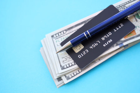 Credit card and pen with US dollar currency money bills banknotes on light blue background....