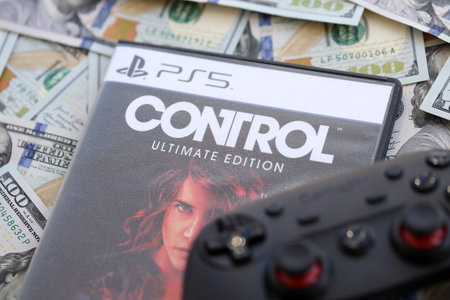 KYIV, UKRAINE - SEPTEMBER 8, 2025 Control videogame lies on big amount of hundred dollar bills with gamepad close upのeditorial素材