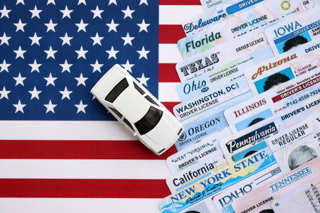 Toy car on big amount of driving licenses from different USA states on flag close up. Stack of...