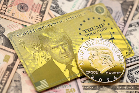 KYIV, UKRAINE - DECEMBER 13, 2025 Trump gold card and souvenir coin on big amount of US dollar money bills banknotes close upのeditorial素材