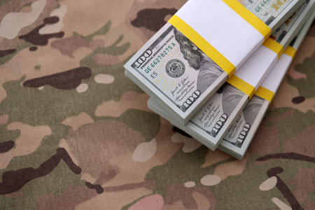 Three packs of ten thousand US dollar bills on camouflage background. Packs of hundred dollar bills...