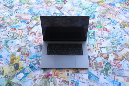 Modern laptop lies on big amount of money bills banknotes from different currencies close up