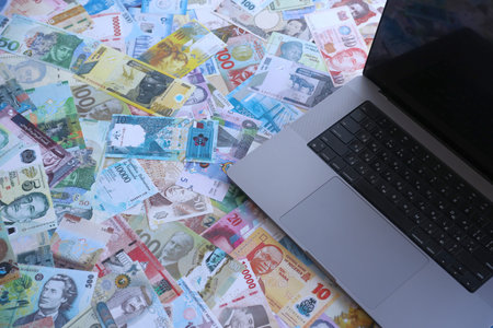 Modern laptop lies on big amount of money bills banknotes from different currencies close up