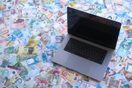 Modern laptop lies on big amount of money bills banknotes from different currencies close upの写真素材