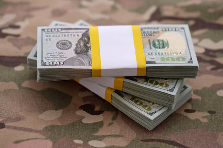 Three packs of ten thousand US dollar bills on camouflage background. Packs of hundred dollar bills...