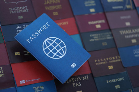 Fictional passport book travel document on big amount of real passport covers of various different countries. Expired passports in big pile close up. Travel documents for tourismの写真素材