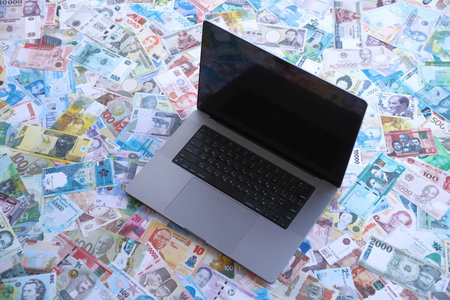 Modern laptop lies on big amount of money bills banknotes from different currencies close up
