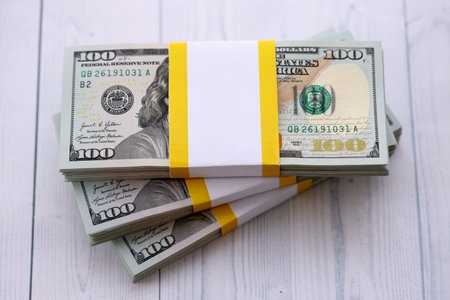 Three packs of ten thousand US dollar bills on wooden background. Packs of hundred dollar bills in...
