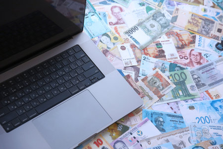 Modern laptop lies on big amount of money bills banknotes from different currencies close up