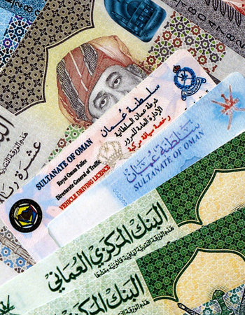 Oman resident card and driving license among Oman rial money bills on table close up. Permanent...